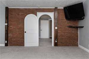 Interior space featuring brick wall, light carpet, and a textured ceiling