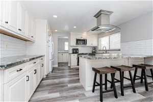 Kitchen featuring white cabinetry, dark stone countertops, a breakfast bar area, backsplash, and light hardwood / wood-style flooring