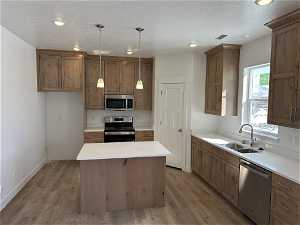 Kitchen with a center island, sink, hardwood / wood-style flooring, decorative light fixtures, and appliances with stainless steel finishes