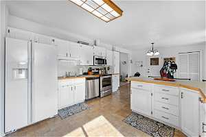 Kitchen featuring a notable chandelier, white cabinetry, appliances with stainless steel finishes, decorative light fixtures, and light tile floors