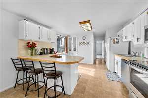 Kitchen with light tile flooring, electric range, a kitchen breakfast bar, and white cabinetry
