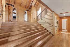 Staircase with light hardwood / wood-style flooring, wooden walls, vaulted ceiling with beams, and wooden ceiling