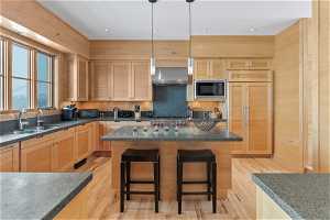 Kitchen featuring hanging light fixtures, wall chimney exhaust hood, a kitchen island, and built in appliances
