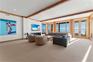 Carpeted living room with a water view, beamed ceiling, and french doors
