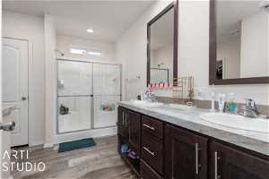 Bathroom with dual sinks, an enclosed shower, vanity with extensive cabinet space, and wood-type flooring