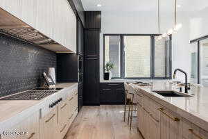 Kitchen featuring light wood-type flooring, backsplash, a kitchen bar, hanging light fixtures, and sink