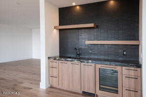 Bar with light brown cabinetry, sink, wood-type flooring, and decorative backsplash