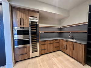 Kitchen featuring stainless steel double oven, light hardwood / wood-style flooring, beverage cooler, and sink