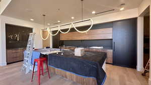 Interior space featuring a kitchen bar, kitchen peninsula, decorative light fixtures, light hardwood / wood-style flooring, and dark stone countertops