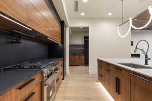 Kitchen with sink, high end range, light hardwood / wood-style floors, custom range hood, and dark stone counters