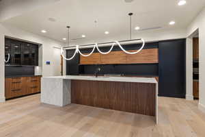 Kitchen with an island with sink, sink, pendant lighting, and light hardwood / wood-style flooring