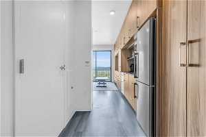 Kitchen with light brown cabinetry, hardwood / wood-style floors, and stainless steel fridge