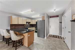 Kitchen featuring kitchen peninsula, appliances with stainless steel finishes, light tile floors, and backsplash