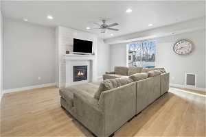 Living room featuring brick wall, light hardwood / wood-style floors, a fireplace, and ceiling fan