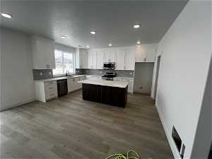 Kitchen with light hardwood / wood-style floors, a kitchen island, white cabinets, sink, and stainless steel appliances
