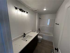 Full bathroom featuring a textured ceiling, vanity, wood-type flooring, bathtub / shower combination, and toilet