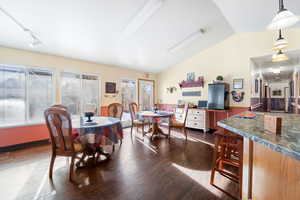 Dining area with dark hardwood / wood-style floors, vaulted ceiling, and track lighting