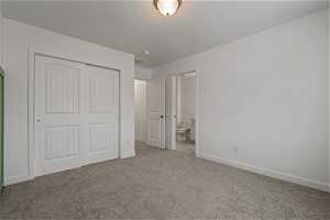 Unfurnished bedroom featuring light colored carpet, ensuite bathroom, and a closet