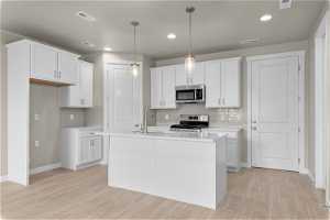 Kitchen with stainless steel appliances, white cabinetry, light wood-type flooring, and an island with sink