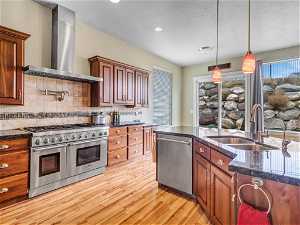 Kitchen with stainless steel appliances, tasteful backsplash, hanging light fixtures, wall chimney range hood, and sink