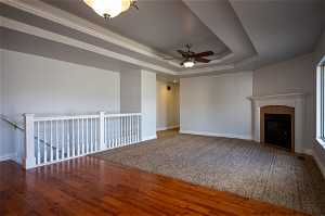 Unfurnished living room with a tiled fireplace , ceiling fan, and a tray ceiling