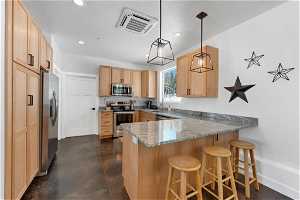 Kitchen with light stone counters, a breakfast bar area, hanging light fixtures, kitchen peninsula, and appliances with stainless steel finishes
