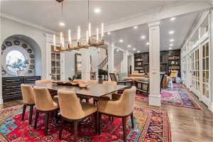 Dining area with dark hardwood / wood flooring, crown molding, built in shelves, and decorative columns
