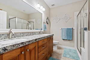 Bathroom with an enclosed shower and bench, toilet, tile flooring, double sink, and vanity with extensive cabinet space