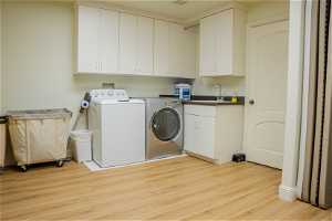 Laundry room with cabinets, sink, washing machine and clothes dryer, and light wood-type flooring