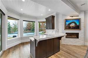 Kitchen with light hardwood / wood-style floors, light stone countertops, ornamental molding, and a breakfast bar area