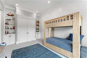 Carpeted bedroom with a closet, wood walls, and ornamental molding