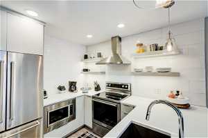 Kitchen with backsplash, white cabinets, hanging light fixtures, fume extractor, and built in appliances