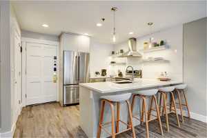 Kitchen with tasteful backsplash, light wood-type flooring, fume extractor, and stainless steel fridge