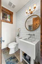 Bathroom featuring tile walls, a chandelier, toilet, tile floors, and sink