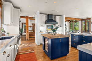Kitchen with blue cabinetry, wall chimney range hood, white cabinets, and butcher block counters