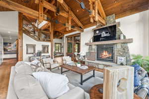 Living room with wooden ceiling, hardwood / wood-style floors, a stone fireplace, beam ceiling, and high vaulted ceiling