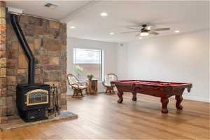 Playroom featuring light hardwood / wood-style floors, billiards, beamed ceiling, ceiling fan, and a wood stove