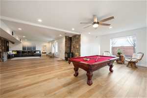 Recreation room featuring light hardwood / wood-style floors, pool table, ceiling fan, and a wood stove