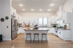Kitchen with white cabinetry, a kitchen island, a breakfast bar area, backsplash, and high quality appliances