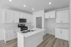 Kitchen featuring white cabinetry, a center island with sink, appliances with stainless steel finishes, light hardwood / wood-style flooring, and sink