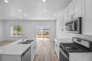 Kitchen with a textured ceiling, light wood-type flooring, white cabinetry, sink, and stainless steel appliances