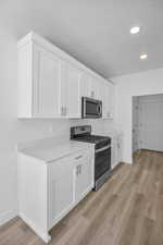 Kitchen with a textured ceiling, stainless steel appliances, light wood-type flooring, and white cabinets