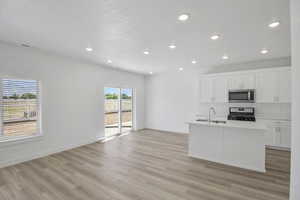 Living Room, Dining room, and Kitchen with a kitchen island with sink, light wood-type flooring, white cabinets, range, and sink