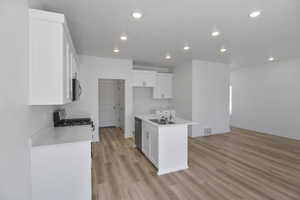 Kitchen with light wood-type flooring, white cabinets, sink, an island with sink, and stainless steel appliances