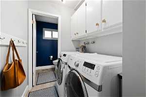 Clothes washing area featuring washing machine and clothes dryer, light hardwood / wood-style floors, and cabinets