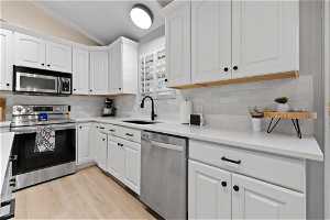 Kitchen with light wood-type flooring, stainless steel appliances, white cabinets, sink, and vaulted ceiling