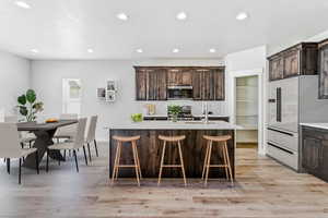 Kitchen featuring light wood-style floors, dark brown cabinets, recessed lighting, light countertops, and a breakfast bar area