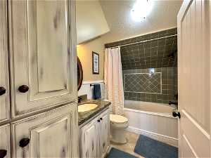 Full bathroom with shower / bath combination with curtain, toilet, vanity with extensive cabinet space, tile flooring, and a textured ceiling