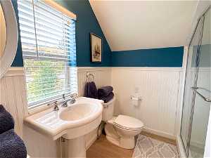 Bathroom above detached garage featuring a shower with shower door, vaulted ceiling, toilet, and LVP-style flooring