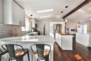 Kitchen with vaulted ceiling with skylight, backsplash, dark wood-type flooring, white cabinetry, and pendant lighting